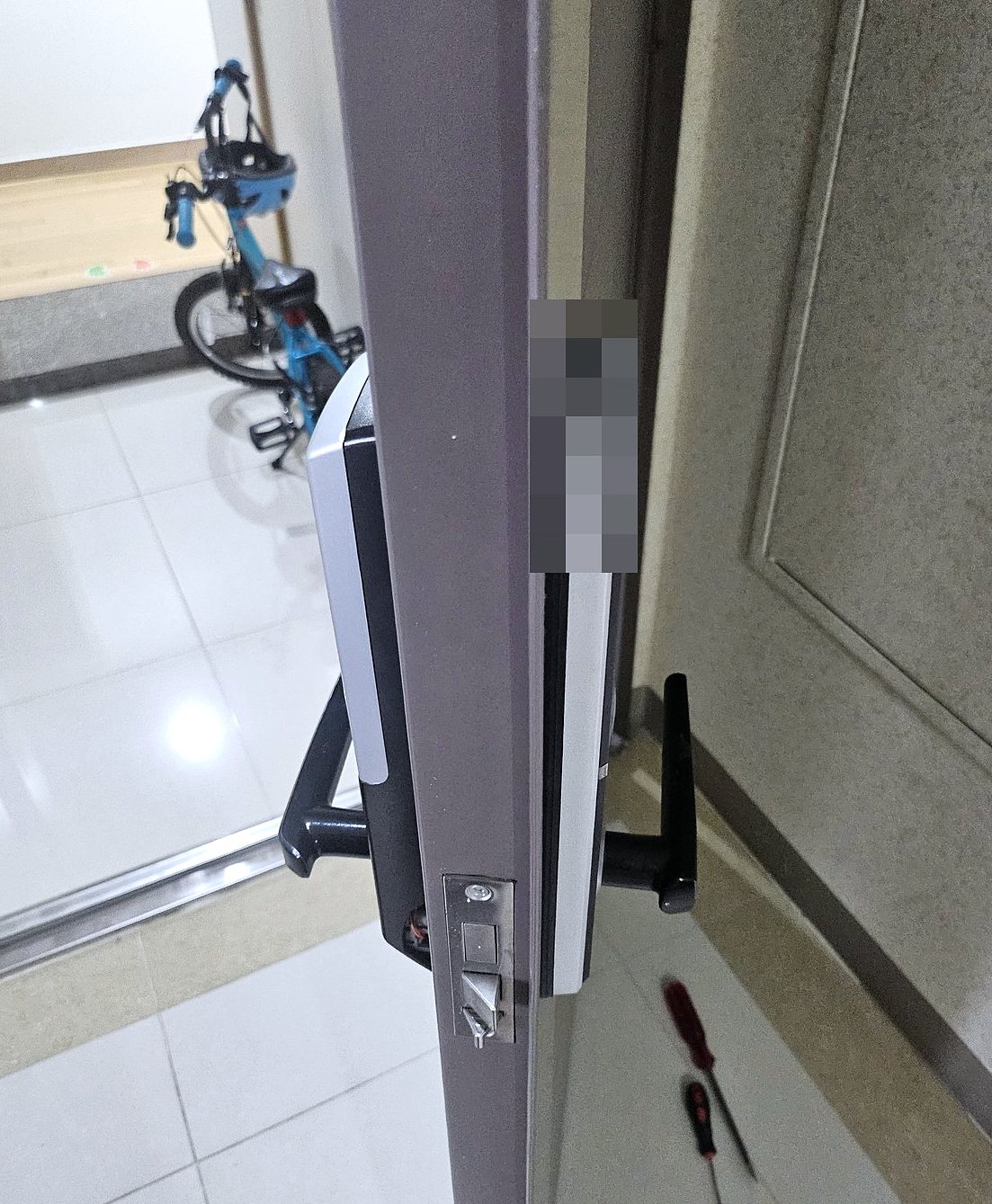 군포시 궁내동 출장 — 열린 문 가장자리의 잠금 막대와 안팎 도어락, 바닥의 드라이버 두 자루, 복도의 파란 자전거